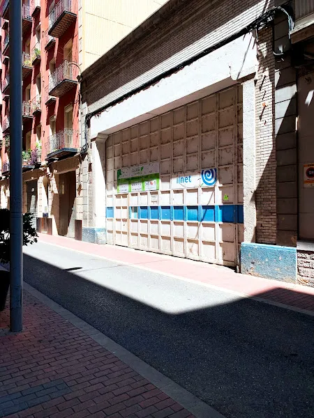 Puerta metálica cerrada de la deixalleria lestacio lleida punt net en una calle estrecha con aceras y balcones