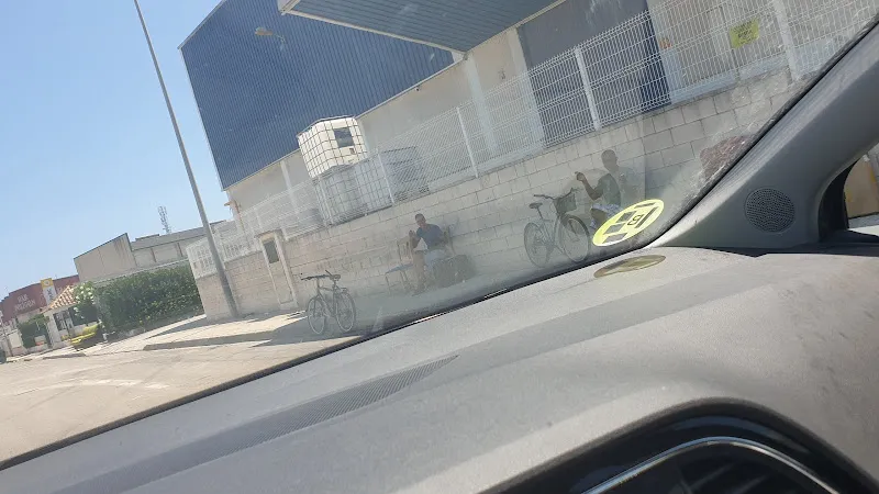 Vista desde el interior de un coche hacia una fachada urbana con bicicletas y personas cerca de un ecoparque
