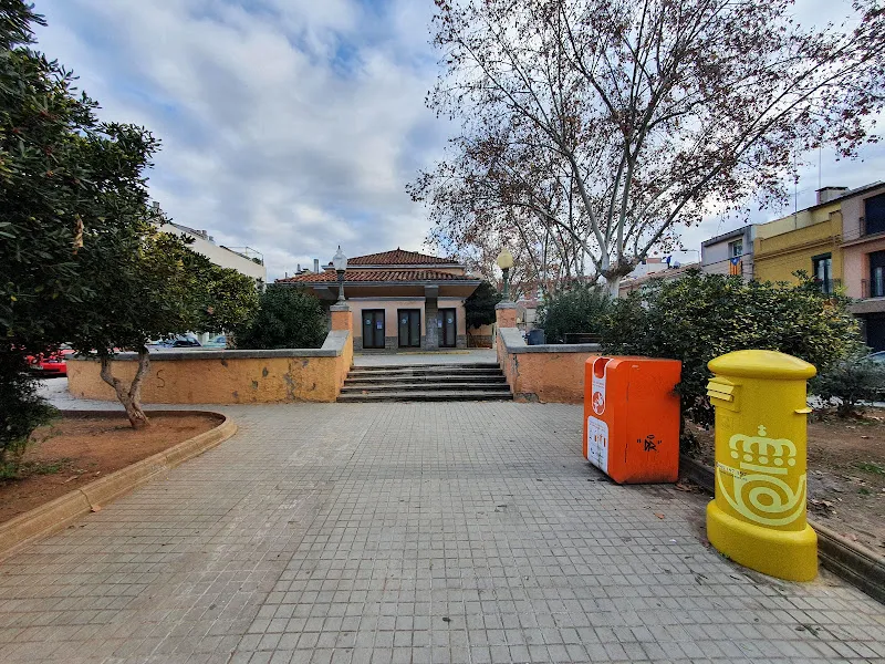 Plaza con escalones, árboles y contenedores naranja y amarillo junto a un punt de recollida d oli usat