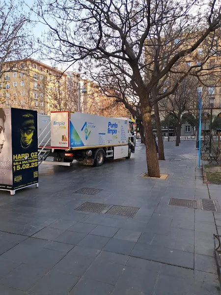 Camión rotulado Punto limpio estacionado en una plaza arbolada junto a edificios, punto limpio movil universidad.