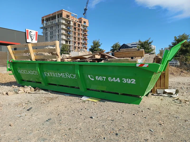 Contenedor verde lleno de escombros y madera con la marca reciclados extremenos s l.