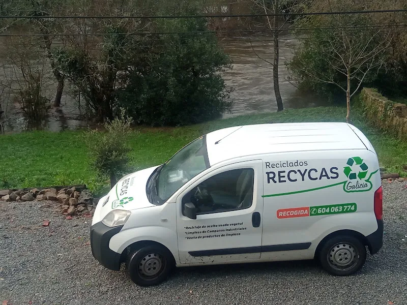 Furgoneta blanca de reciclados recycas con logo de reciclaje estacionada sobre grava cerca de un río.